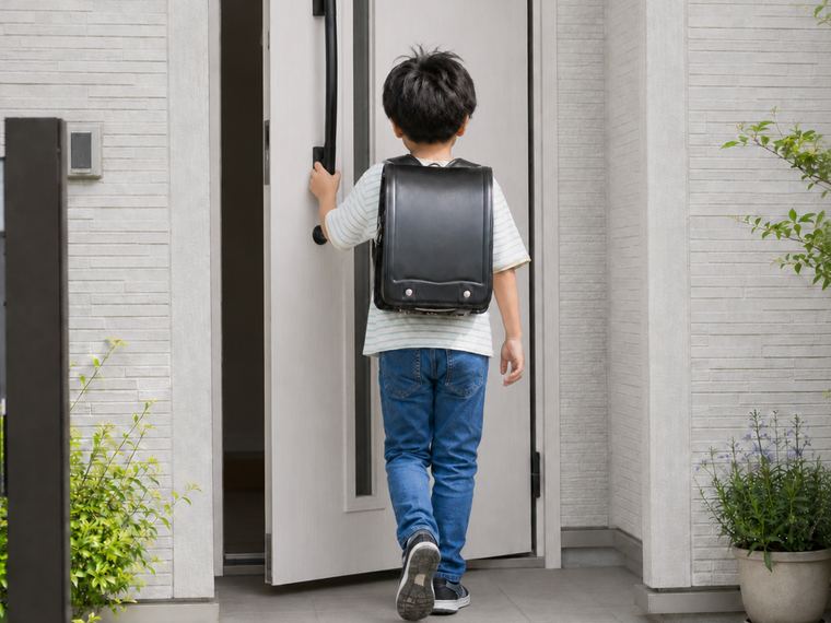 ランドセルを背負った子どもが玄関ドアを開けて家に入る様子